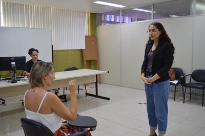 Imagem: Michele (sentada) e Laura (em pé) fazem prova prática de Libras